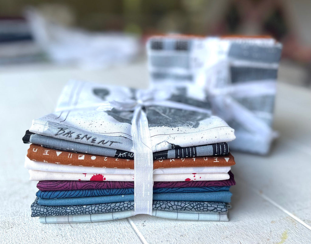 a stack of Sleuth Fabric Bundles by Giucy Giuce fabrics on top of a table from Andover Fabrics.