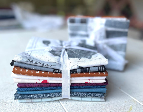 A stack of Sleuth Fabric Bundles by Giucy Giuce from Andover Fabrics on top of a table.